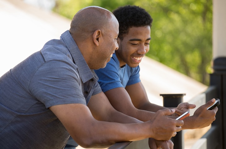 A man and a teen talk while holding their phones