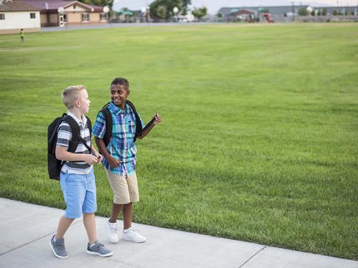 Two diverse school kids walking home together after school and talking together. Back to school photo of  diverse school children wearing backpacks in the school yard