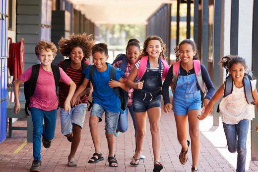 A group of middle school students wearing backpacks smiling and running down a school hall together.